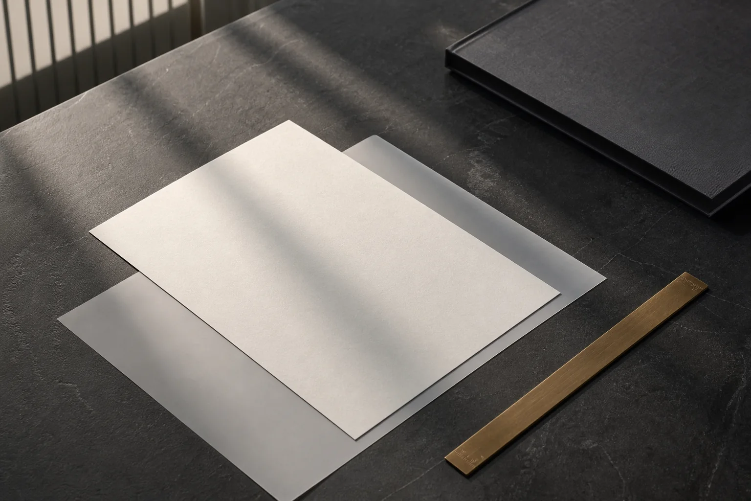 Blank vellum, a graphite portfolio and a brass rule arranged on a stone worktable